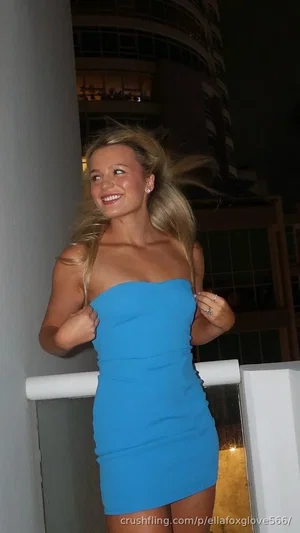 Blonde woman in blue strapless dress standing on balcony at night.