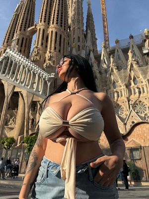 Woman in beige top and jeans poses outdoors in front of large cathedral.