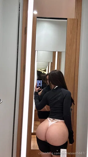 Woman in black long-sleeve top and black shorts with white underwear visible, taking mirror selfie