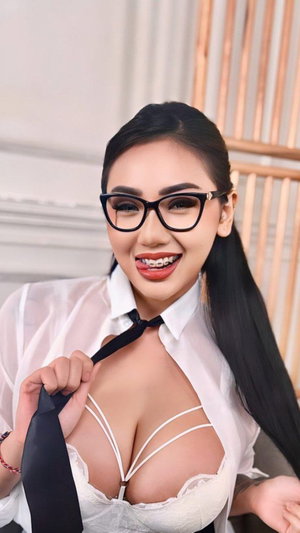 Woman with long black hair wearing glasses, white sheer shirt, and white lingerie holding a tie
