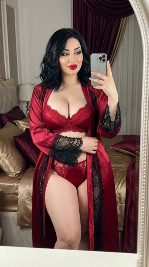 Woman in red lace lingerie and robe takes mirror selfie in bedroom.