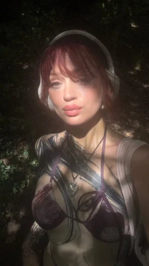Woman with red hair wearing a dark bra and tank top, standing outdoors at night with trees behind