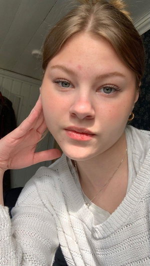 Woman with light brown hair and blue eyes wearing a white sweater indoors.