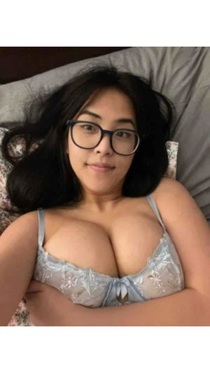Woman with dark hair and glasses lying in bed, wearing light blue lace lingerie.