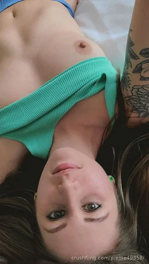 Woman with tattooed arm lying on bed, wearing teal top, face up, dark hair.