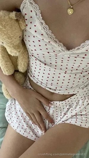 Woman in white heart-patterned pajamas holding teddy bear, lying on bed.