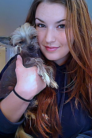 Woman with long brown hair holding a small dog indoors.