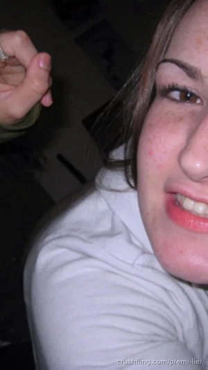 Woman with freckles and brown hair in a white top, smiling in a close-up selfie.