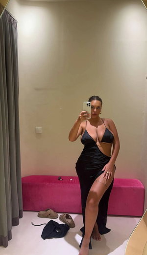 Curvy woman in black dress taking mirror selfie indoors.