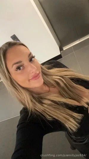 Woman with long blonde hair in black top, smiling in indoor setting.