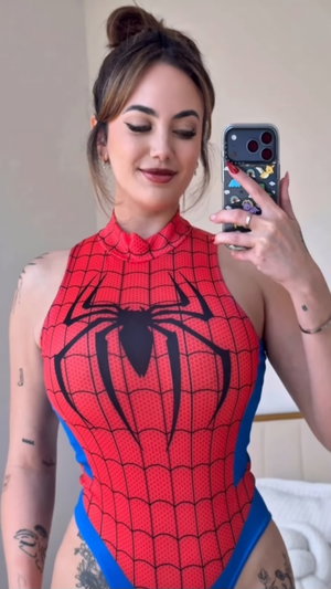 Curvy woman in red Spider-Man bodysuit, mirror selfie indoors.