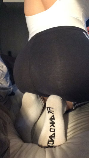 Curvy woman in white top, black leggings on bed.