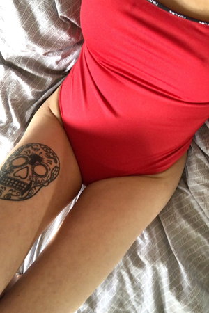 Woman in red bodysuit with skull tattoo on bed.