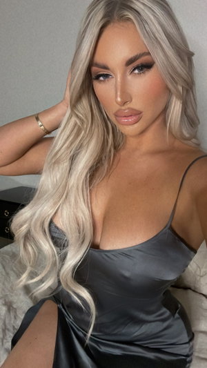 Woman with long blonde hair in a gray satin dress posing indoors.