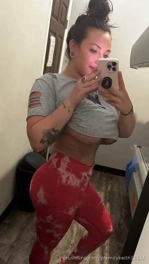 Woman in gray crop top and red tie-dye leggings taking mirror selfie indoors.