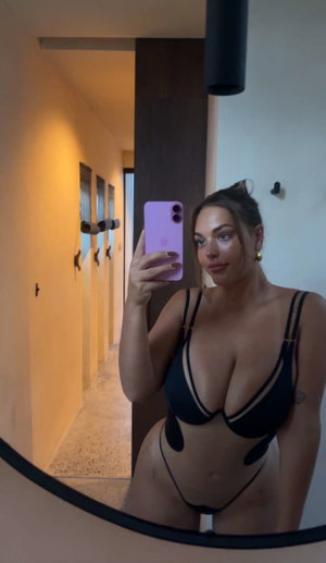 Woman in black lingerie taking mirror selfie in hallway.