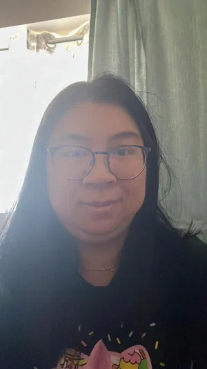 Woman with long dark hair and glasses wearing a black graphic t-shirt indoors.