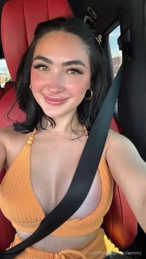Woman with dark hair in orange top sitting in red car seat, smiling at camera.