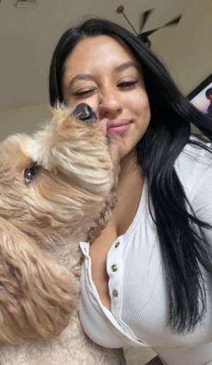 Woman with long dark hair posing with dog in white top.