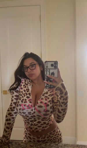 Curvy woman in leopard print outfit taking mirror selfie indoors.