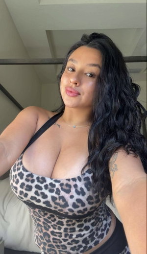 Woman with long dark hair in leopard print top, taking selfie indoors.