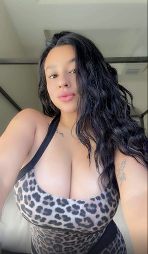 Woman with long black hair in leopard print top, indoors, tattoos visible.