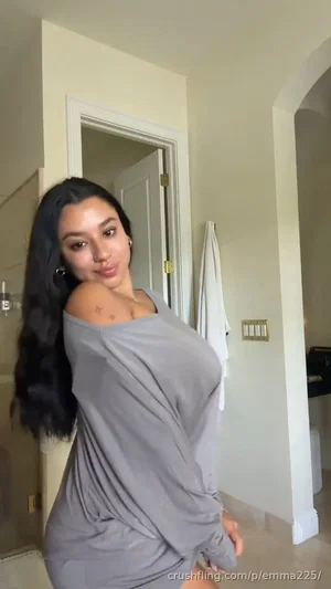 Woman with long dark hair in a gray off-shoulder dress posing indoors.