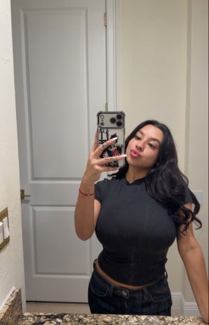 Curvy woman with long dark hair taking mirror selfie indoors.