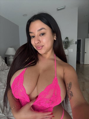 Woman with long dark hair wearing pink lace lingerie in bedroom.