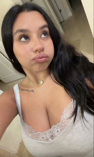 Woman with long dark hair in white lace top indoors.
