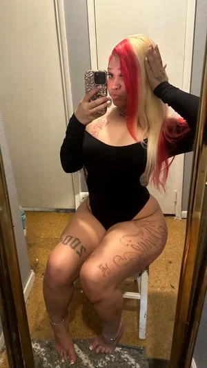 Curvy woman with red-blonde hair in black bodysuit mirror selfie.