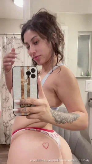 Woman in light gray top and red-trim underwear takes mirror selfie in bathroom.