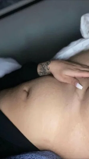 Person with tattooed hand and long nails resting on bare stomach, wearing black top.