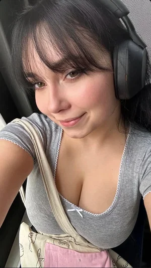 Woman with dark hair wearing gray top and headphones, sitting in a car.