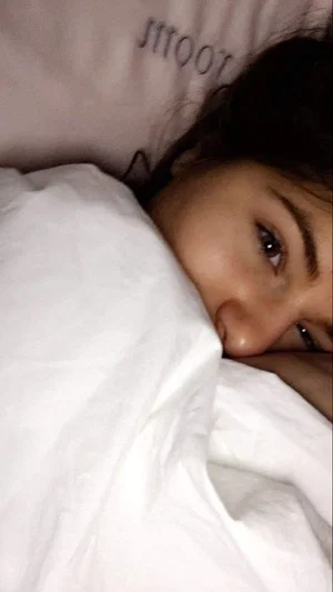Woman with dark hair lying in bed under white covers.