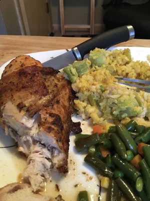 Plate of roasted chicken, rice with avocado, and green beans on wooden table.
