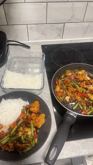 Kitchen scene with cooked stir-fry and rice on plate and in glass container.