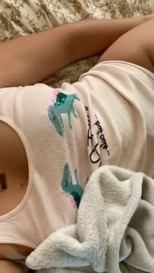 Woman in light pink tank top with dinosaur print lying on patterned bedspread, towel nearby.