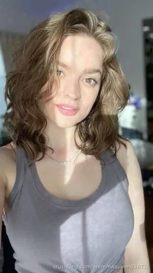 Woman with wavy brown hair wearing a gray tank top indoors.