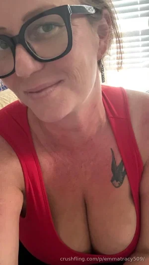 Woman with glasses and red tank top, tattoo on chest, indoor setting.