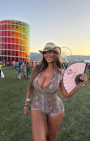 Woman in snakeskin bodysuit and hat at outdoor festival.