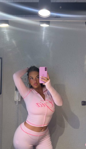 Woman in pink athletic wear taking mirror selfie indoors.
