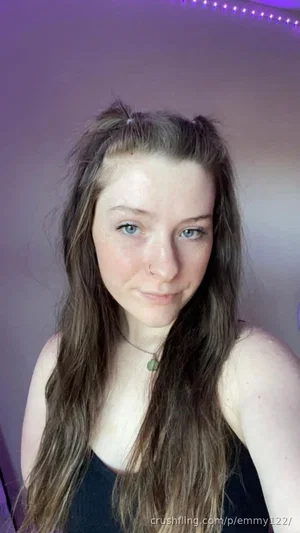 Woman with long brown hair and blue eyes, wearing a black top, in a room with purple LED lights.