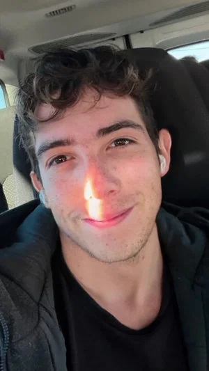 man with curly hair wearing black shirt and jacket inside car