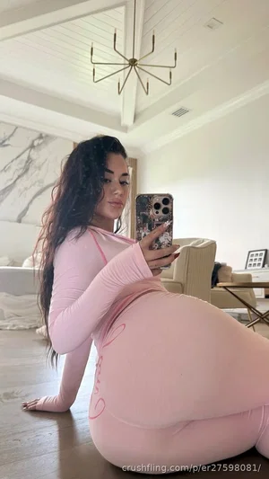 Woman in pink bodysuit taking mirror selfie in bedroom, long dark hair, curvy figure.