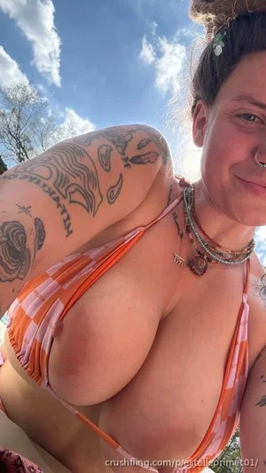 Woman with tattoos in orange bikini top outdoors under blue sky.