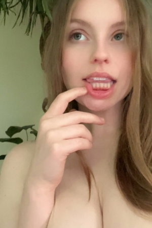 Blonde woman touching lips topless indoors.