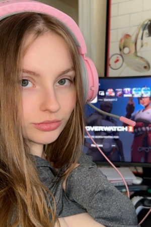 Woman in gray hoodie and pink headphones at gaming desk.