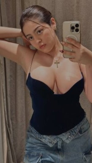 Woman in black top and denim shorts takes mirror selfie indoors.