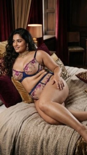 Woman in floral lingerie posing on bed in dimly lit bedroom.
